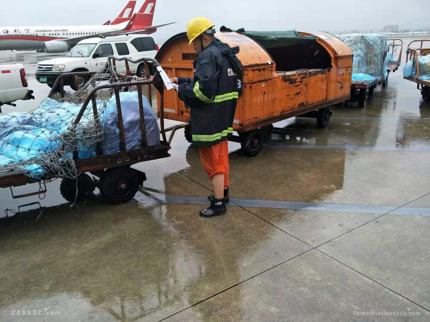 東航虹橋裝卸服務(wù)中心員工正在風(fēng)雨中核對(duì)拖車中裝載的行李和貨物清單。供圖/東航